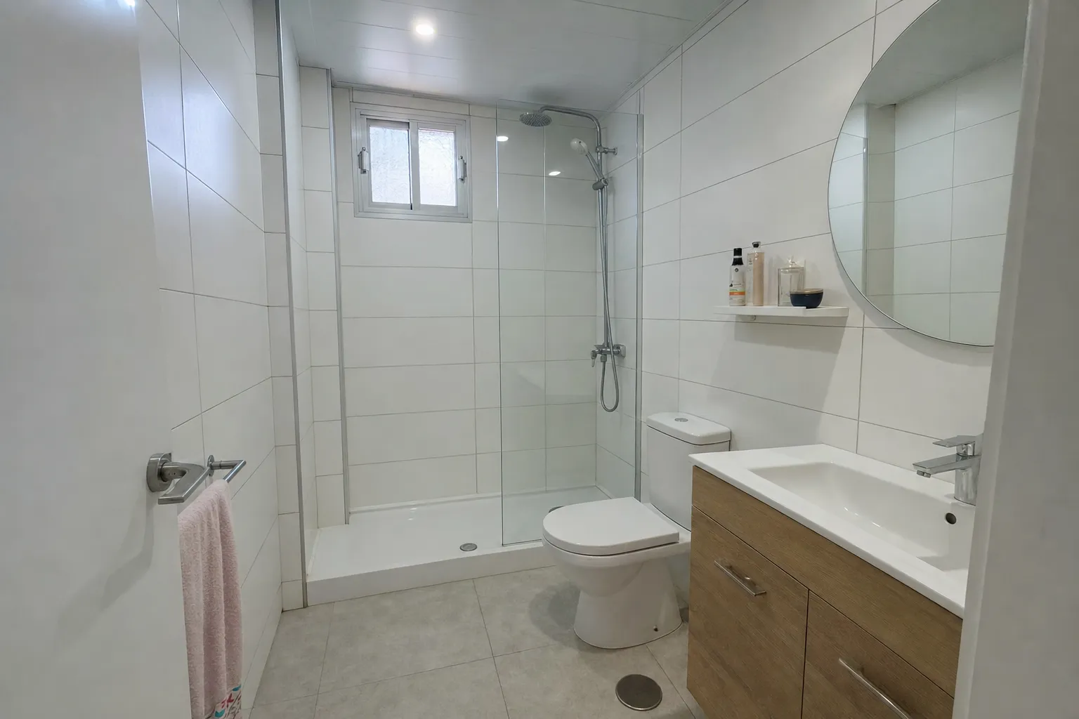 Baño reformado en Estepona con alicatado blanco, mueble flotante de roble y mampara de cristal