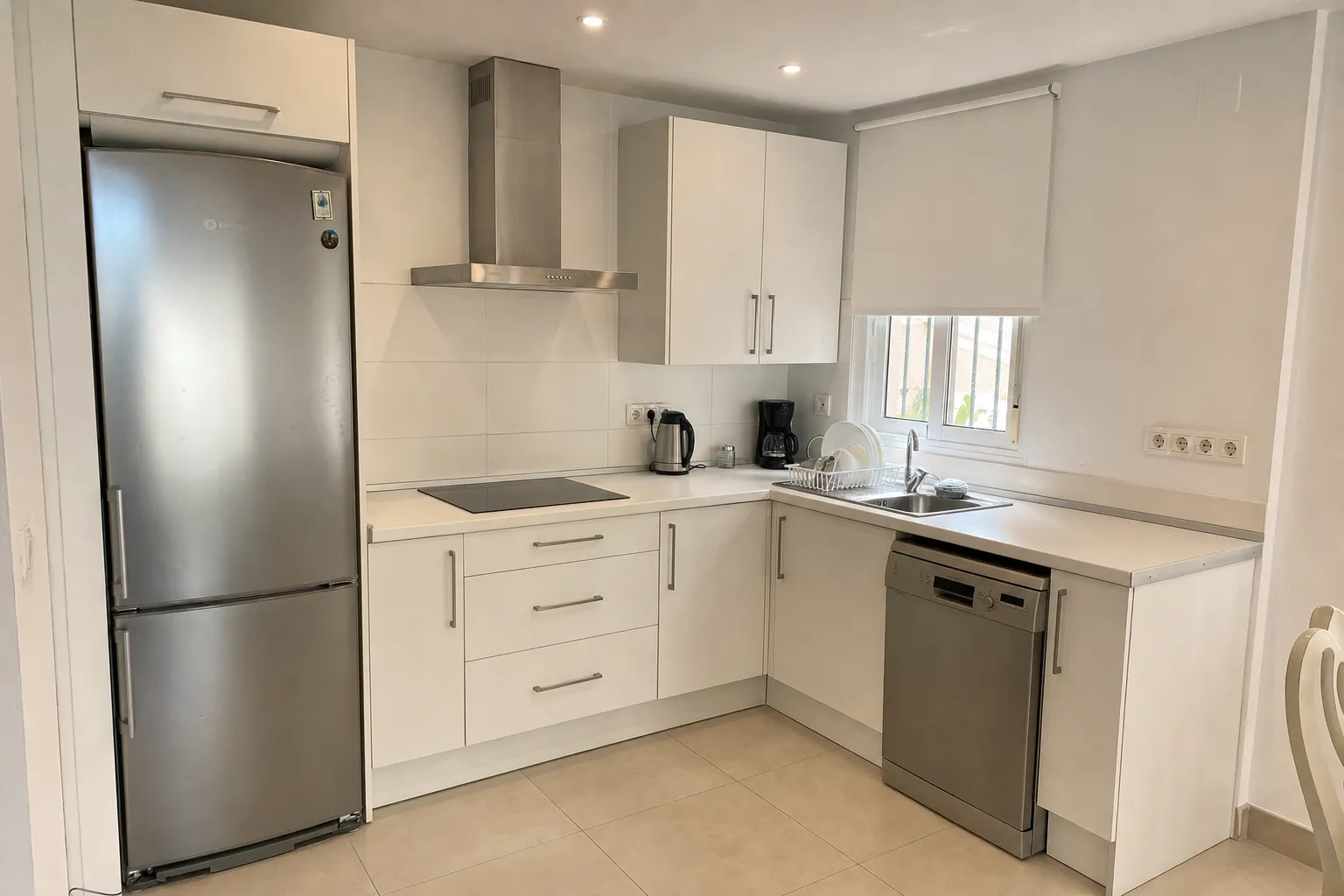 Cocina reformada con muebles blancos y electrodomésticos de acero inoxidable